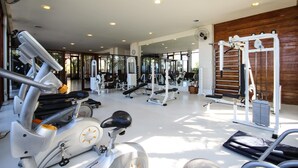 Een fitnessruimte met diverse trainingsapparaten, waaronder loopbanden, hometrainers en krachtapparaten.