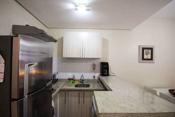 A compact kitchen with a stainless steel refrigerator, a sink, and white cabinets.