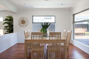 A dining area with a wooden table and chairs, a large wall clock, and a window with blinds.