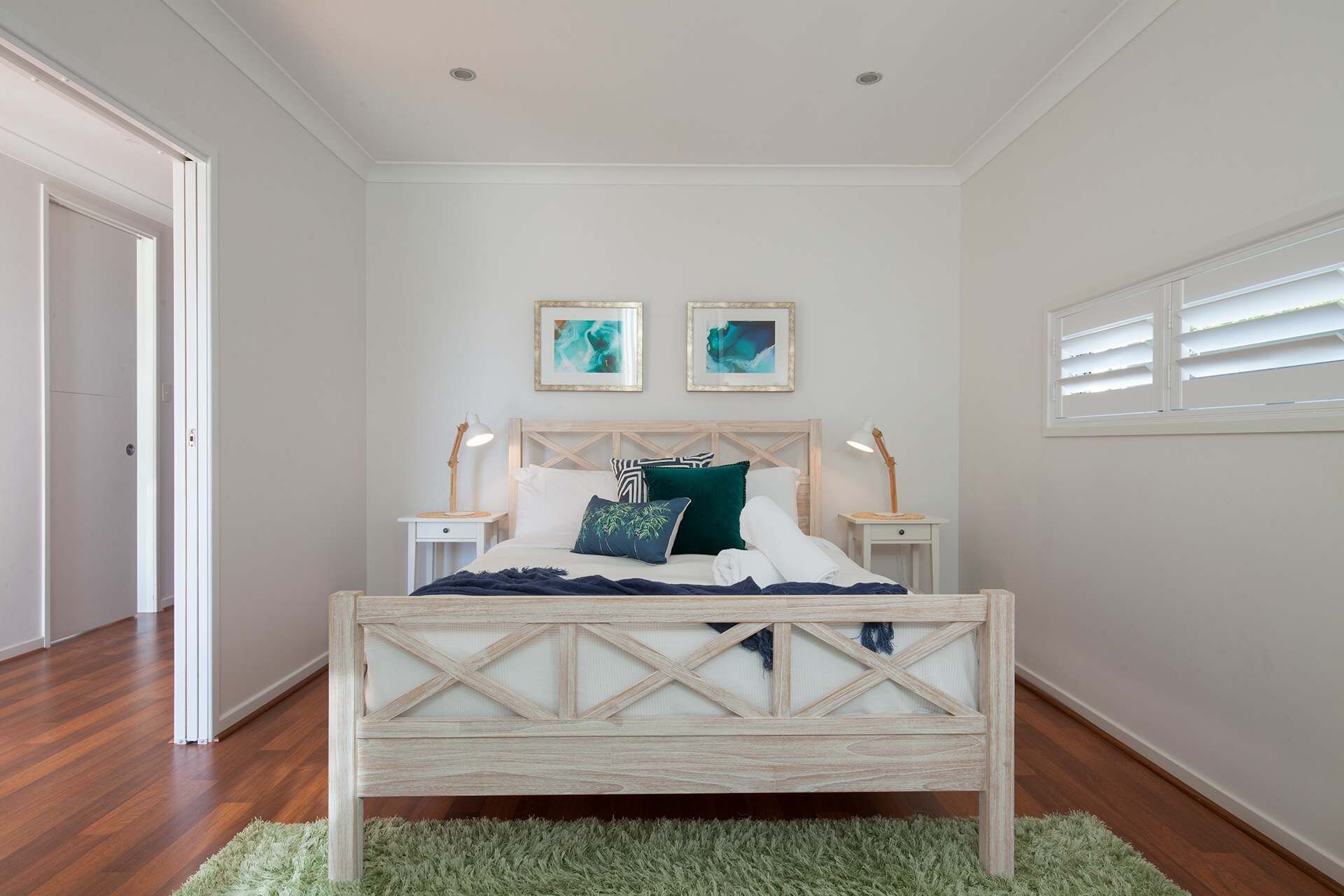 A bedroom with a wooden bed, white walls, two bedside lamps, and a green rug.