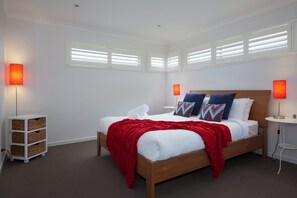 A modern hotel room with a wooden bed, white bedding, red throw, and two bedside lamps.