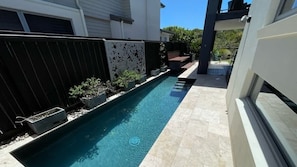 A swimming pool with a black fence, potted plants, and a patio area.