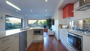 A modern kitchen with a central island, built-in appliances, and large windows. - Green House Pet-Friendly Beach House (Mount Coolum)