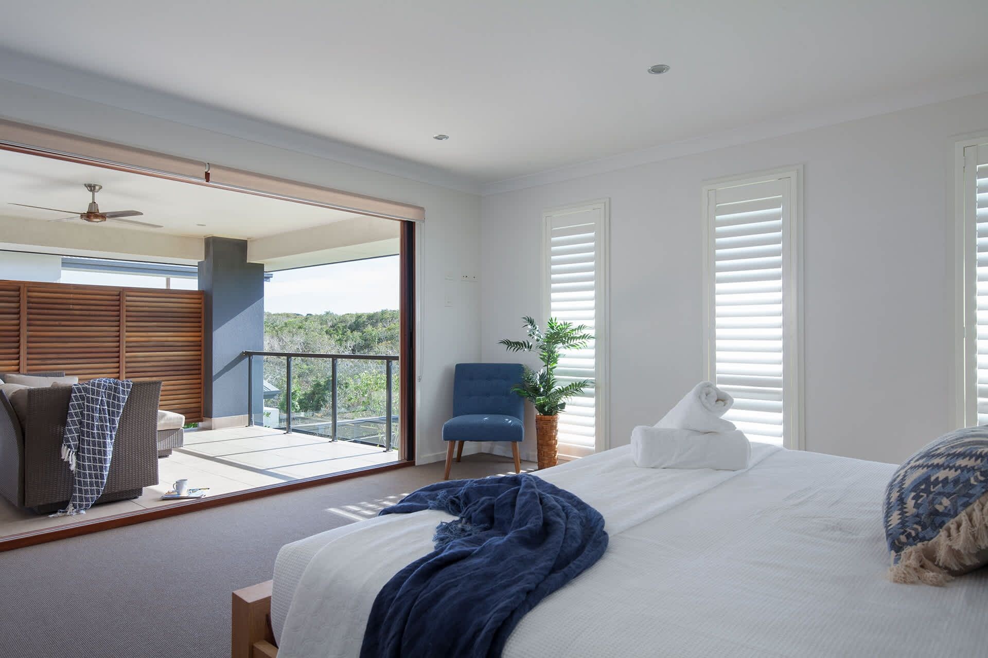 Een slaapkamer met een bed, een stoel, een plant in pot en een balkon met uitzicht.