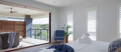 A bedroom with a bed, a chair, a potted plant, and a balcony with a view.