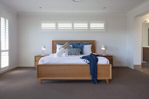 A bedroom with a wooden bed, two bedside tables, a window with blinds, and a mirror.