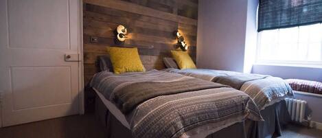 A bedroom with two beds, wooden headboard, wall-mounted lights, and a window with blinds.