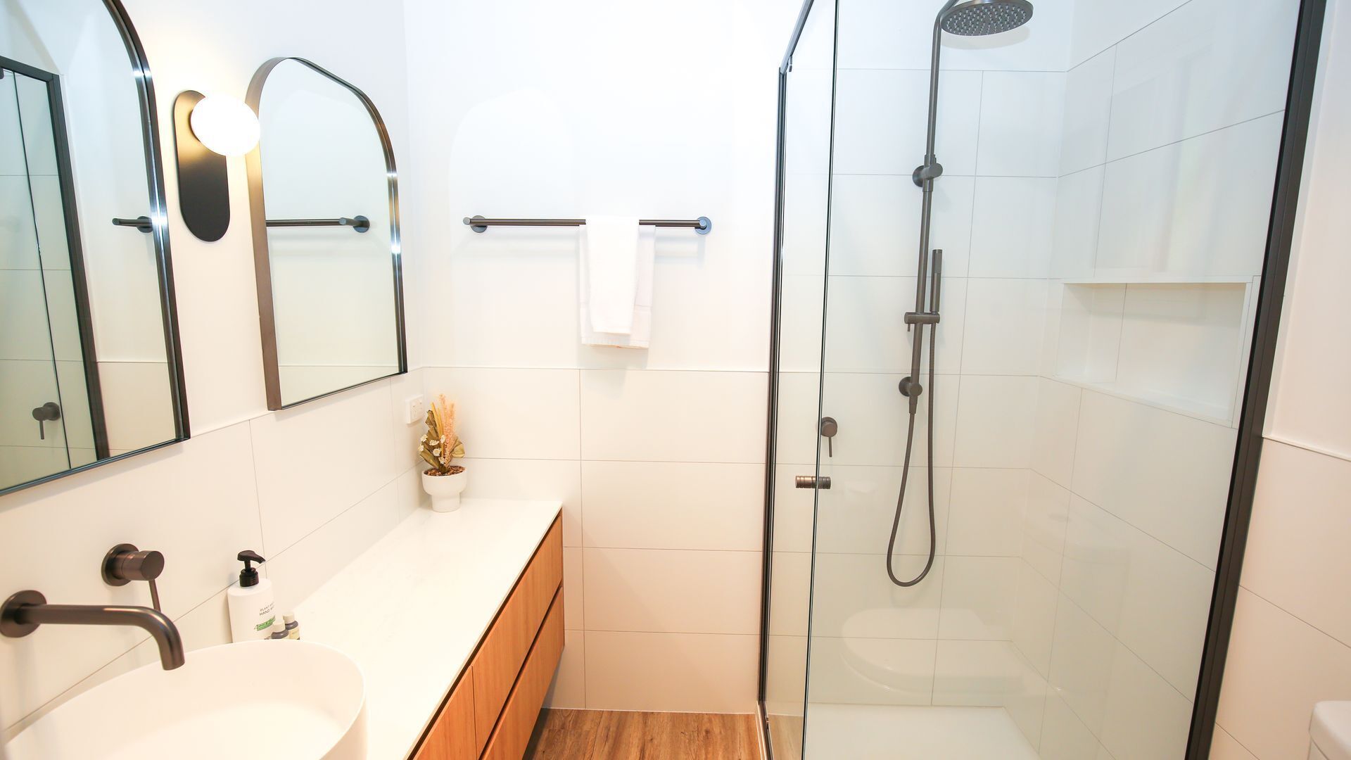 Une salle de bain moderne avec une douche à parois de verre, un lavabo blanc et un meuble-lavabo en bois.