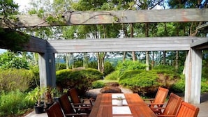 Eine Holzterrasse mit Tisch und Stühlen, umgeben von üppiger Bepflanzung und einer Pergola.