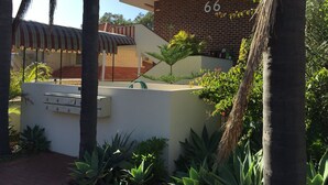 A building with the number 66, surrounded by palm trees and various plants.