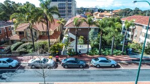A residential area with parked cars, palm trees, and a building with the number 66.