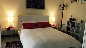 A neatly made bed with white and red bedding, two bedside lamps, a floor lamp, and a bookshelf with books and decorative items. - Clarevale Cottage B&B (Clare)