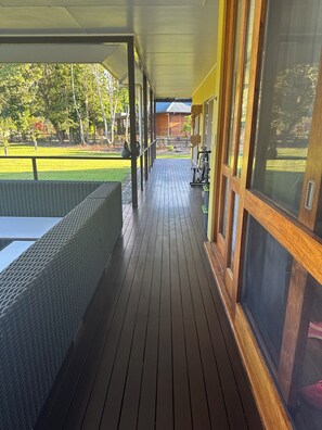 Un espacio al aire libre cubierto con piso de madera, una zona de estar y ventanas amplias.