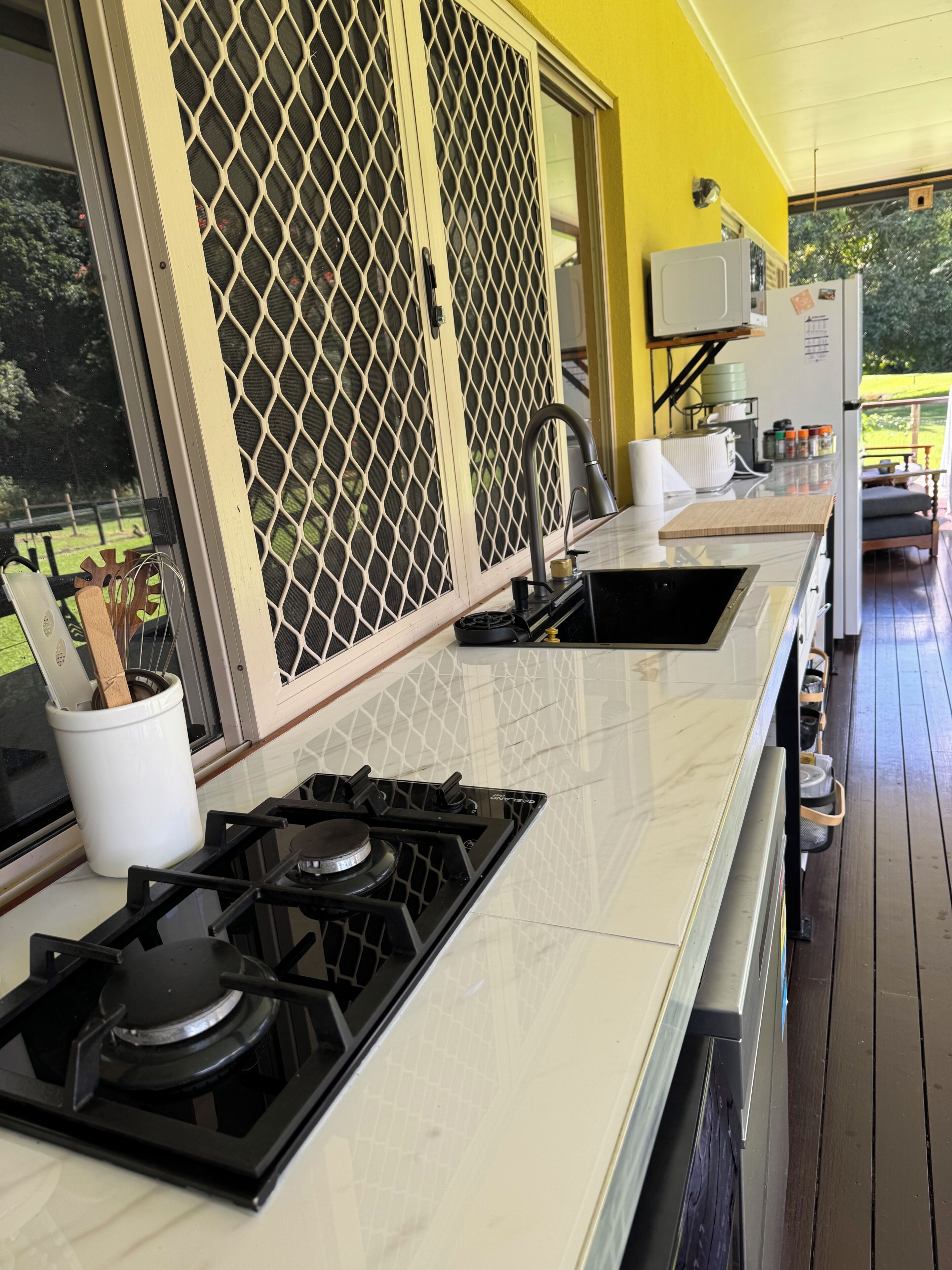 Una cocina con estufa a gas, un lavamanos y un ventanal con mosquitero.