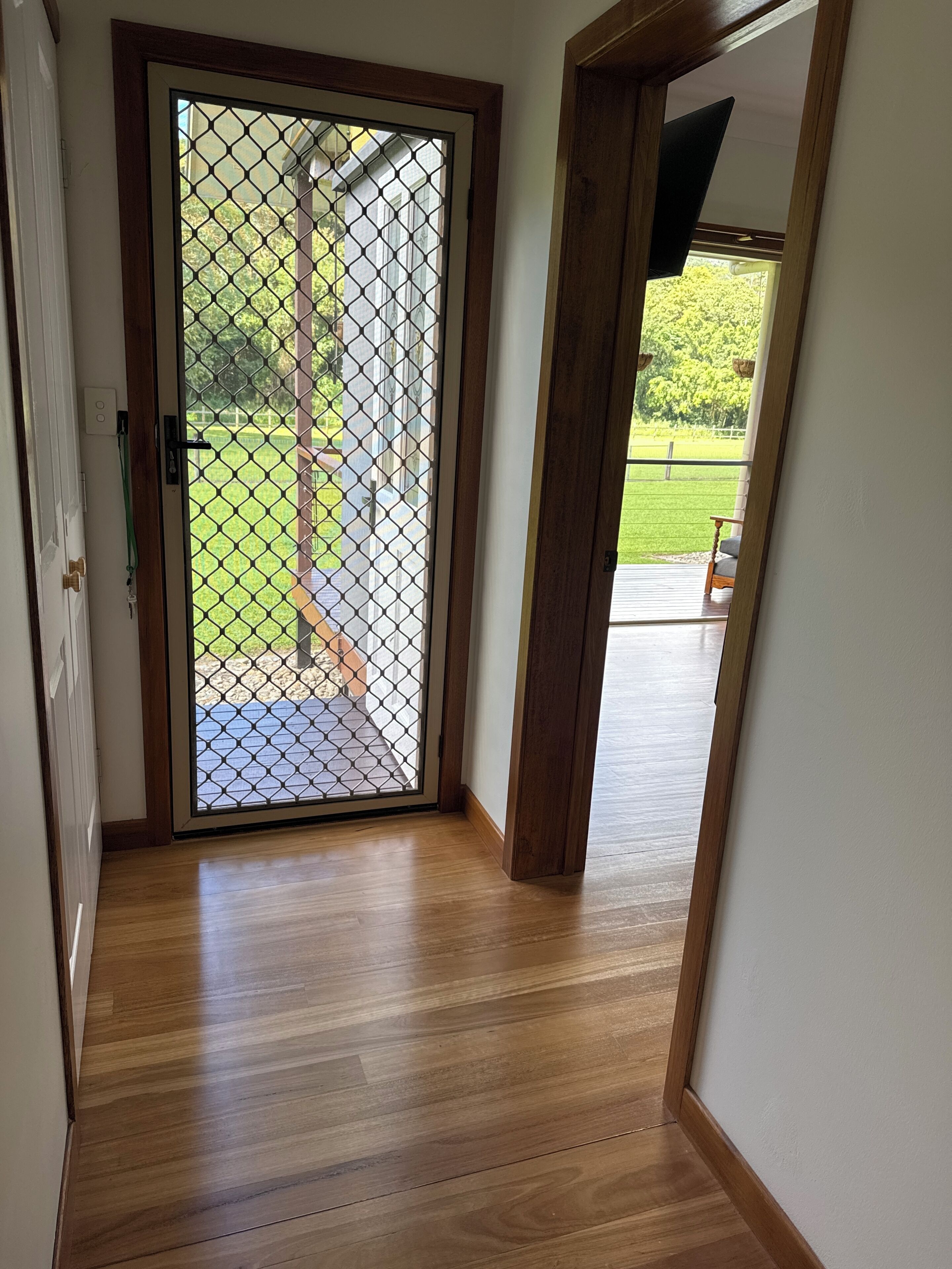 Uma porta de madeira com uma tela de metal, dando acesso a uma área externa com um deck de madeira e vista para uma paisagem verde.