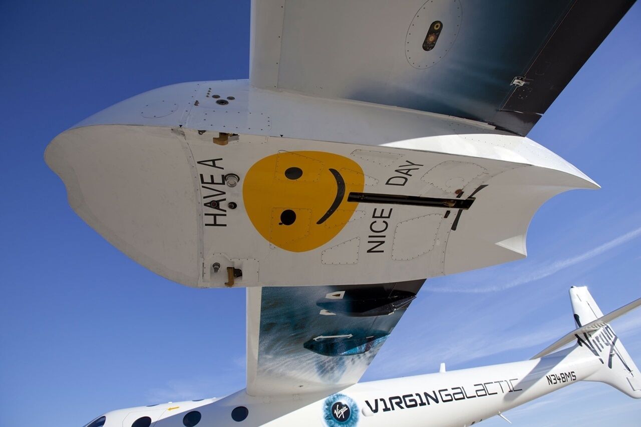 Primer plano del ala de una aeronave Virgin Galactic con el texto "HAVE A NICE DAY" y un caracol sonriente.