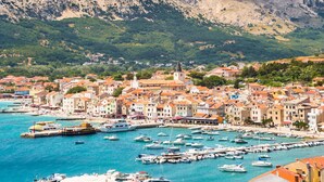 A coastal town with a marina filled with boats, surrounded by buildings with red-tiled roofs and a prominent church spire. - Beachfront, free wi-fi, A/C, free parking (Baška)