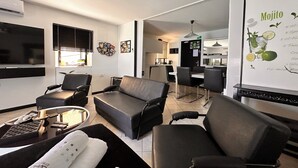 A modern living room with a sofa, chairs, a coffee table, and a TV. There is a dining area with a table and chairs. - Beachfront, free wi-fi, A/C, free parking (Baška)