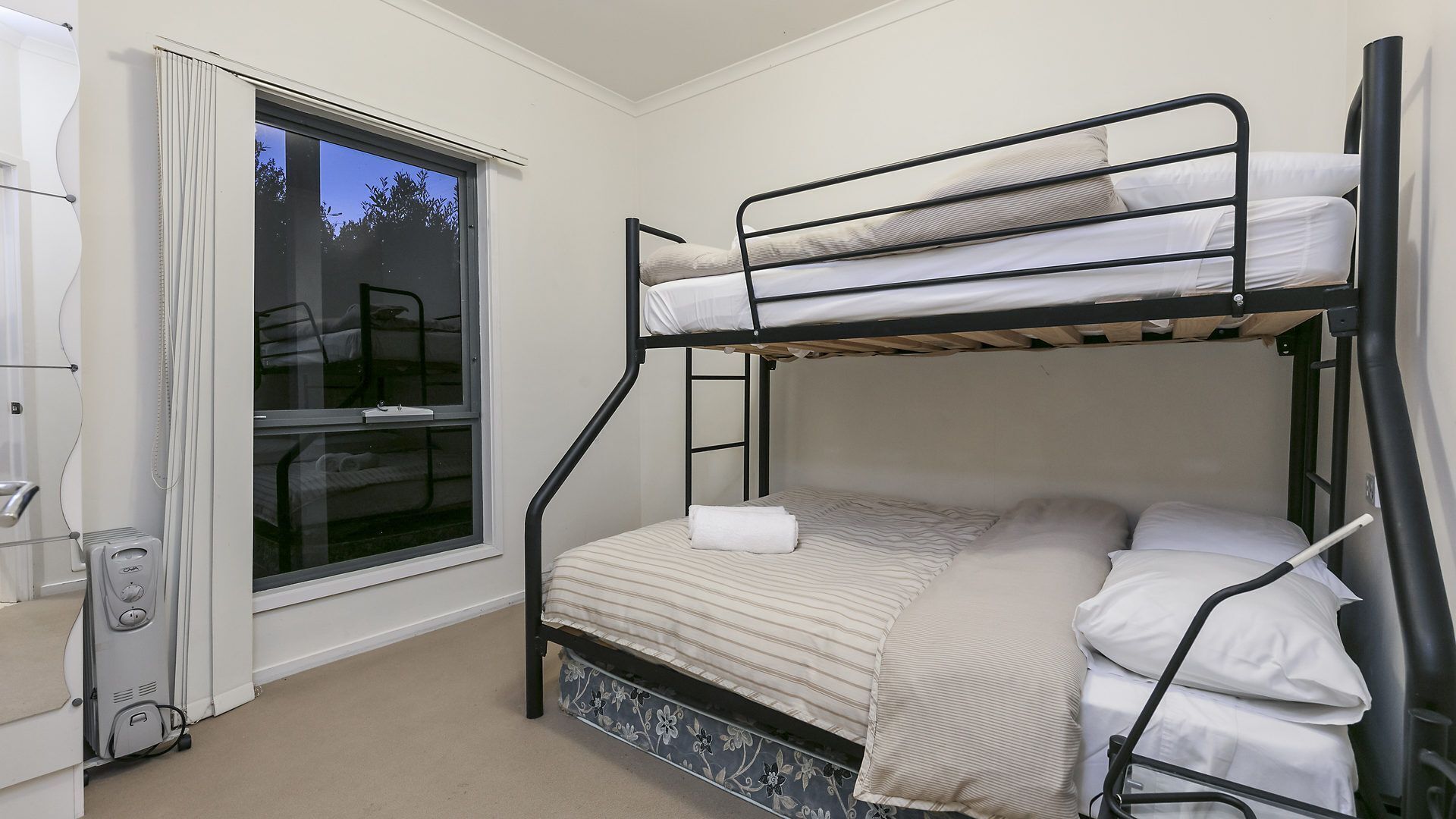 A bunk bed room with a window, a heater, and a small table.