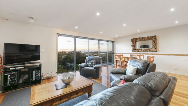 A spacious living room with a large flat-screen TV, leather sofas, a wooden coffee table, and a dining area with wooden chairs and a glass-top table. - Last Minute Discount Available! Moonah Ridge Residence - Perfect for groups. (St Andrews Beach)