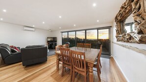 A spacious living area with a wooden dining table and chairs, a black leather sofa, and a large TV. - Last Minute Discount Available! Moonah Ridge Residence - Perfect for groups. (St Andrews Beach)