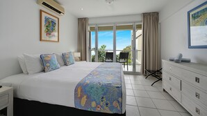 A hotel room with a large bed, a dresser, a ceiling fan, and a balcony with a view. - Ocean View Villa - 02  (Hamilton Island)