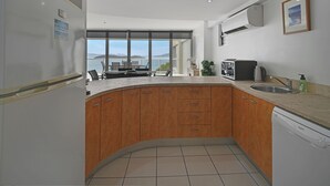 A modern kitchen with wooden cabinets, a built-in dishwasher, and a large window offering a view of the sea. - Ocean View Villa - 02  (Hamilton Island)