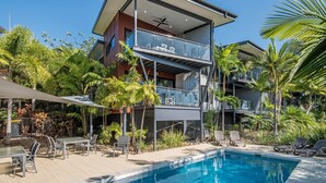 Une maison moderne à deux étages, dotée d’une piscine, de mobilier d’extérieur et d’une végétation luxuriante.