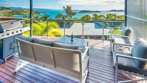 Un balcon équipé d’un barbecue, de sièges et d’une table avec des verres à vin.