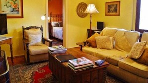 Un salon chaleureux avec un canapé, un fauteuil et une table basse sur laquelle sont posés des livres. Une lampe et un tableau ornent le mur.