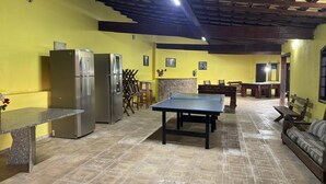 Un espacio interior amplio con mesa de ping pong, sofá, mesa de comedor y zona de cocina con refrigerador y estufa.