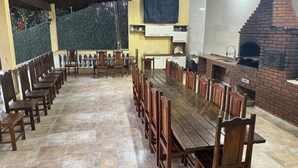 Una larga mesa de madera con sillas, un horno de ladrillo y un piso de baldosas.