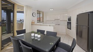 Una cucina moderna con mobili bianchi, un frigorifero in acciaio inossidabile e un'area pranzo con un tavolo in vetro e sedie in vimini.