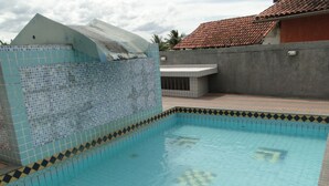 A swimming pool with blue and black tiles, surrounded by a tiled deck and a concrete wall. - Furnished apartment on Itaúna beach, a popular spot for international surfing. (Saquarema)