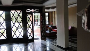 A spacious lobby with a tiled floor, a red sofa, and a view through a lattice door to the outside. - Furnished apartment on Itaúna beach, a popular spot for international surfing. (Saquarema)