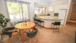Una cocina compacta con gabinetes blancos, microondas y refrigerador. Cuenta con un pequeño comedor con una mesa redonda y cuatro sillas.