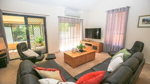 Una sala de estar con un conjunto de sofá, una mesa de centro, un televisor y un ventanal corredero que da a un área exterior.