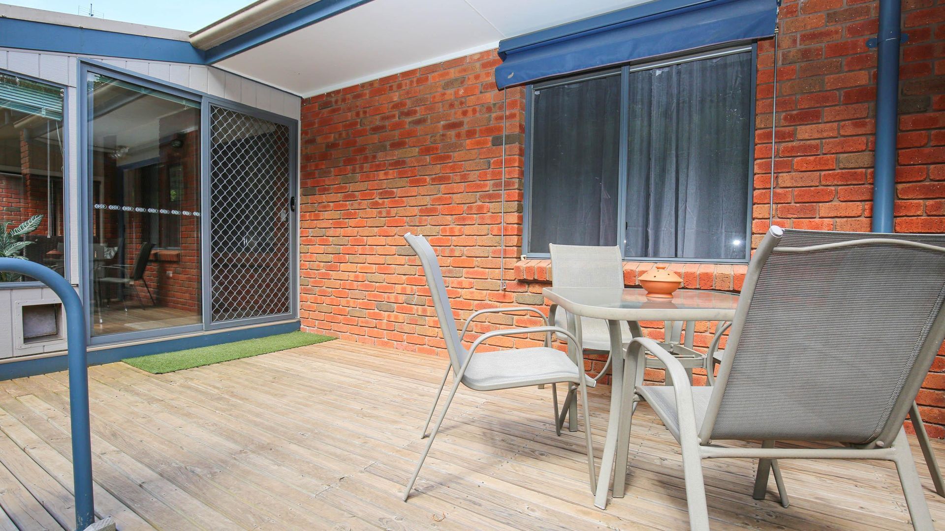 Une terrasse avec une table et des chaises, une porte-fenêtre coulissante et un mur en briques.