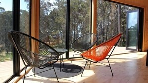 A room with large windows, two chairs, and a small table. - BAY OF FIRES ECO HUT Binalong Bay - Off Grid Experience (Binalong Bay)