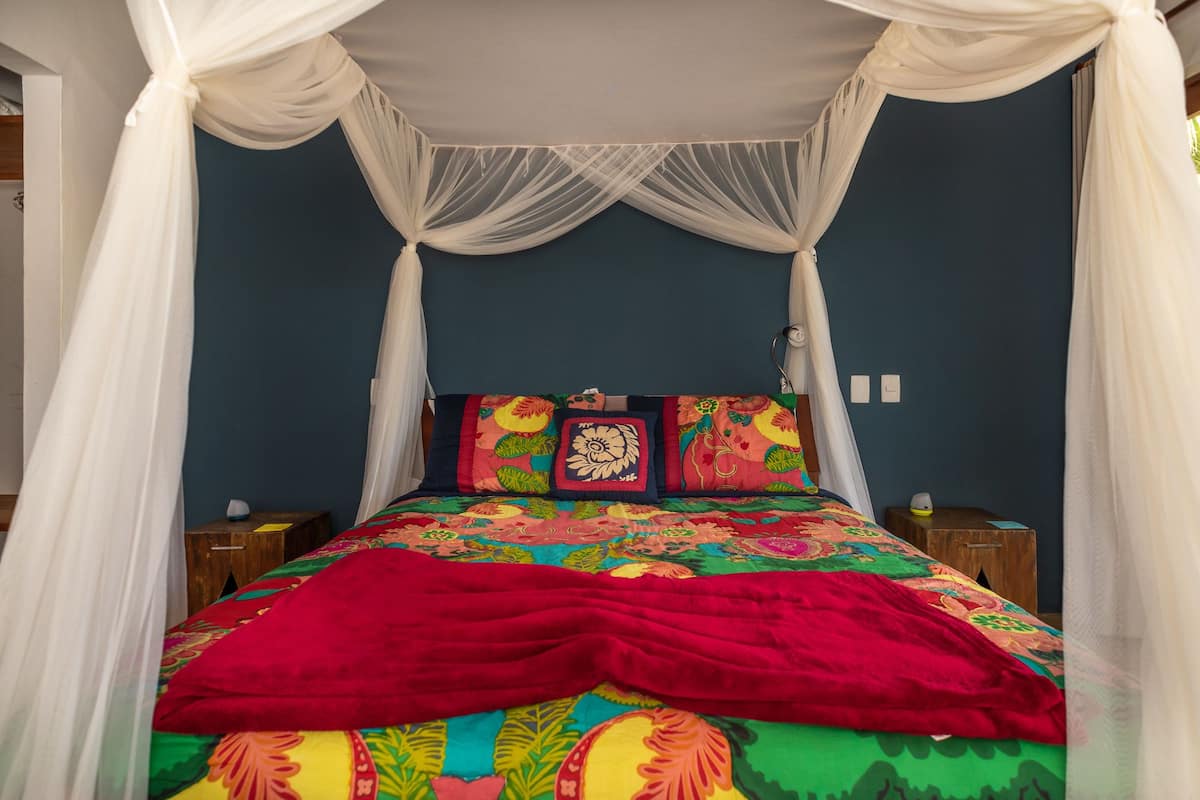 A bed with a colorful bedspread, a red blanket, and a canopy.