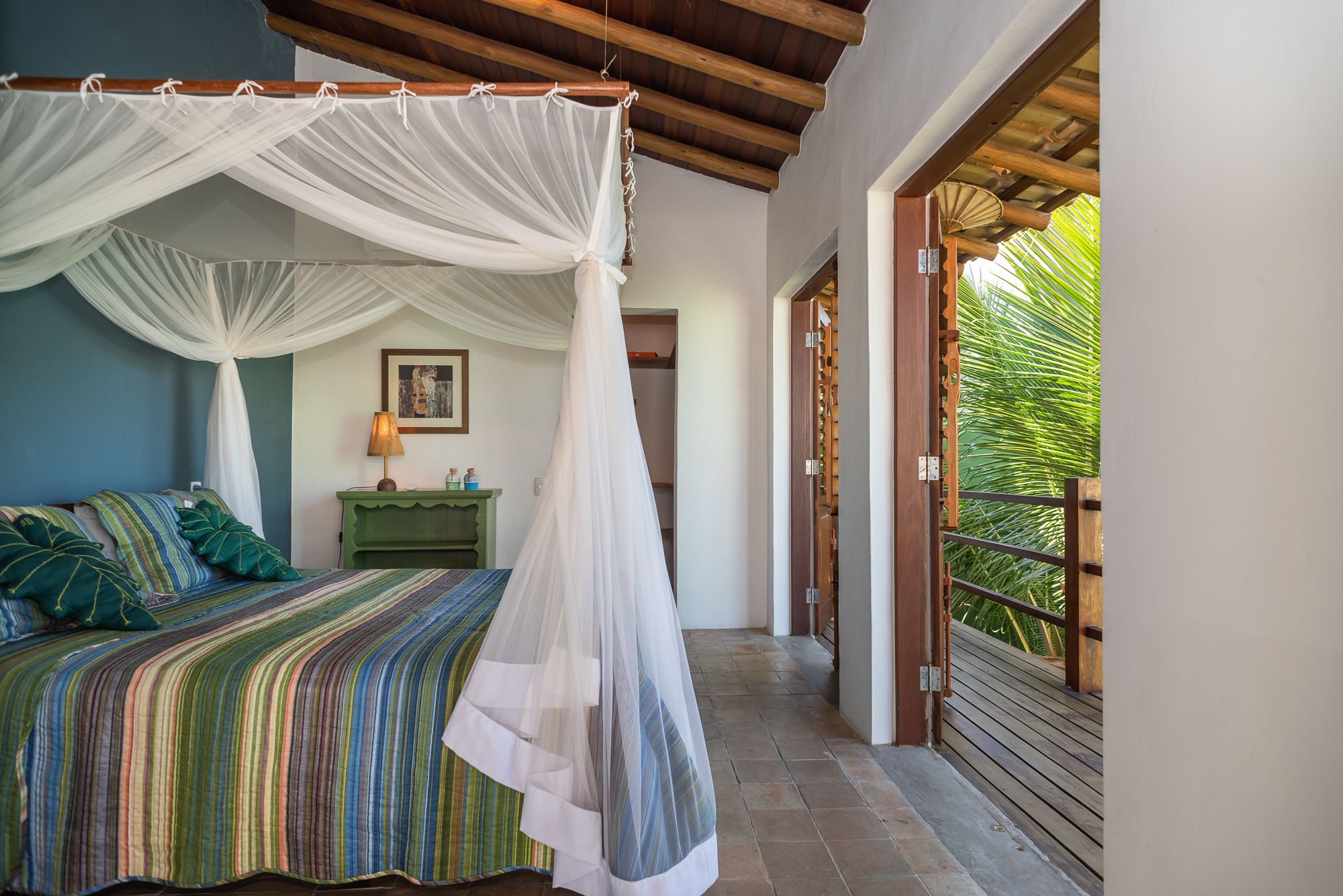 Um quarto com cama, mesa de cabeceira verde, abajur e dossel branco.
