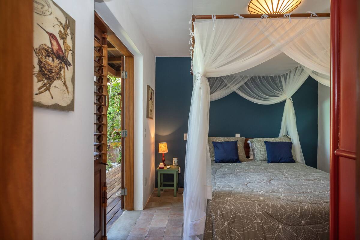 A bedroom with a canopy bed, a small bedside table with a lamp, and a wall-mounted picture.