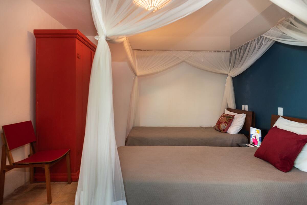 A bedroom with two beds, a red wardrobe, and a chair.
