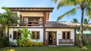 A two-story building with a balcony, wooden shutters, and a tiled roof. - Vila do Outeiro em frente a praça da igreja (Porto Seguro)