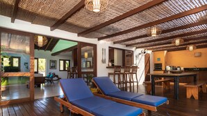 A spacious room with wooden flooring, a dining area with a table and chairs, and a seating area with blue cushioned chairs. - Vila do Outeiro em frente a praça da igreja (Porto Seguro)