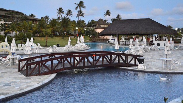 Un espace piscine avec des chaises longues, un pont et une structure à toit de chaume.