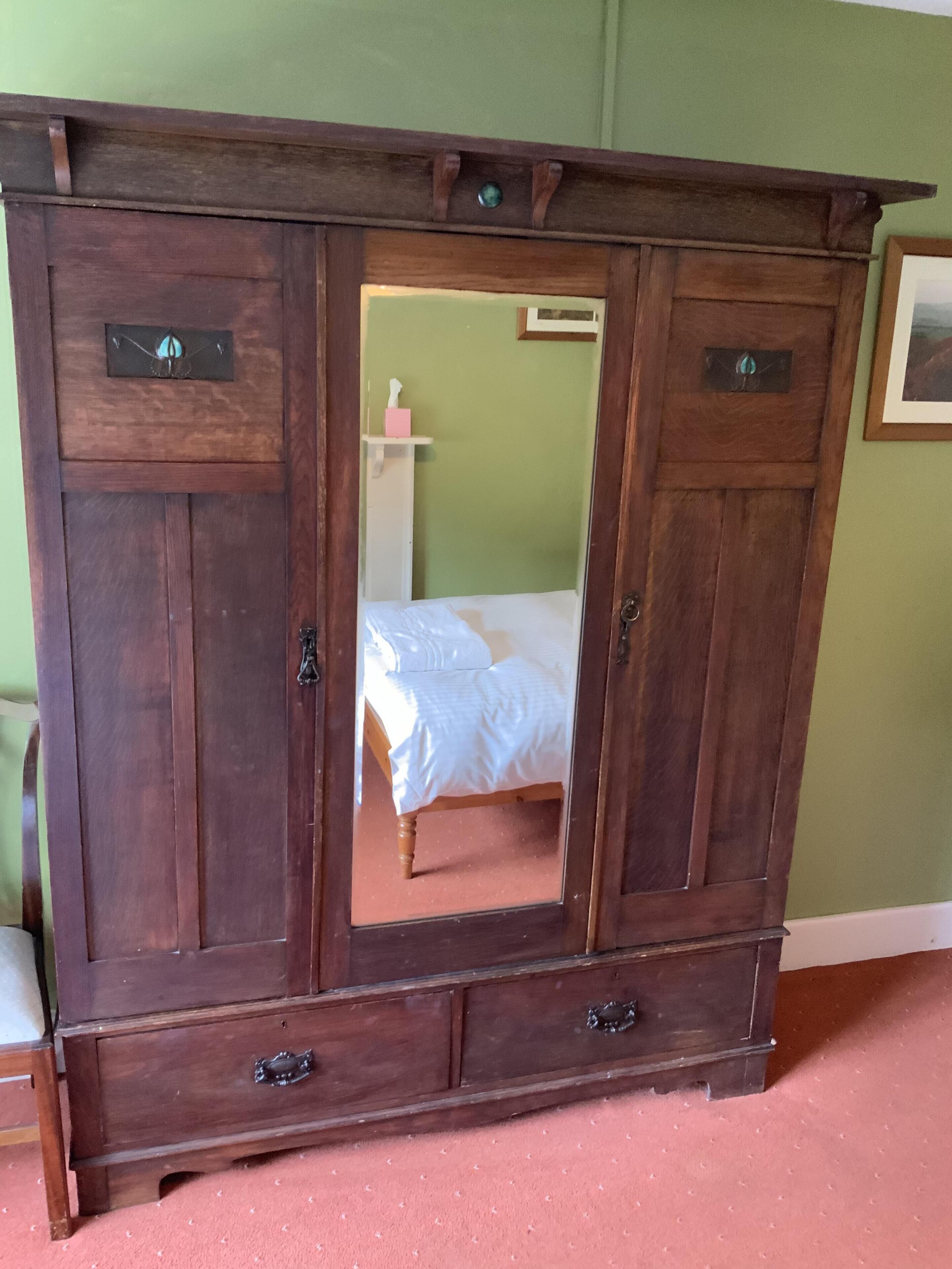 A wooden armoire with a mirror, a bed, and a pink tissue box in the background.