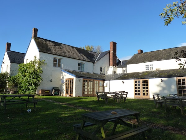 A courtyard with picnic tables and a building with white walls and multiple chimneys. - The Carew Arms (Taunton)