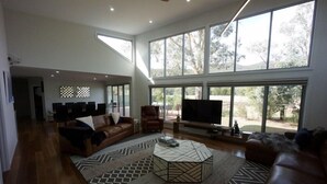 A spacious living room with a large TV, leather sofas, and a geometric coffee table. - Hemley House - Three Bedroom, 2 bathroom House Halls gap (Halls Gap)