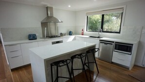 A modern kitchen with a central island, bar stools, a stove, a sink, and a window. - Hemley House - Three Bedroom, 2 bathroom House Halls gap (Halls Gap)